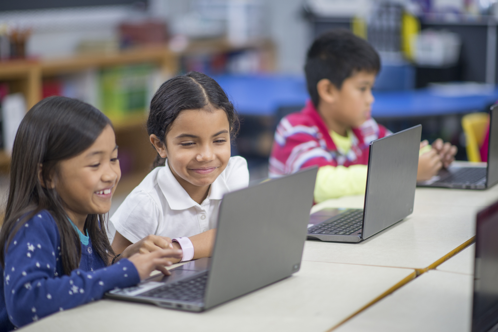 A multi-ethnic group of elementary age students are working together on laptops in the computer lab.