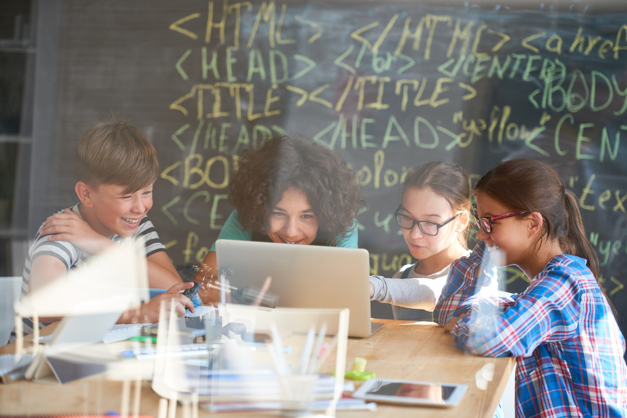 Group of positive teenagers using laptop to learn coding together